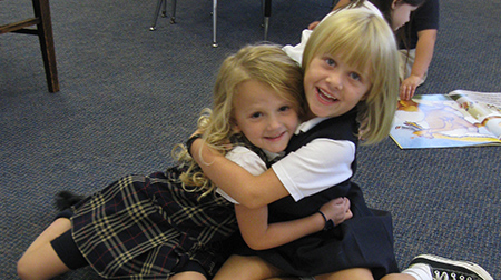 Two small girls hugging, both wearing school uniforms